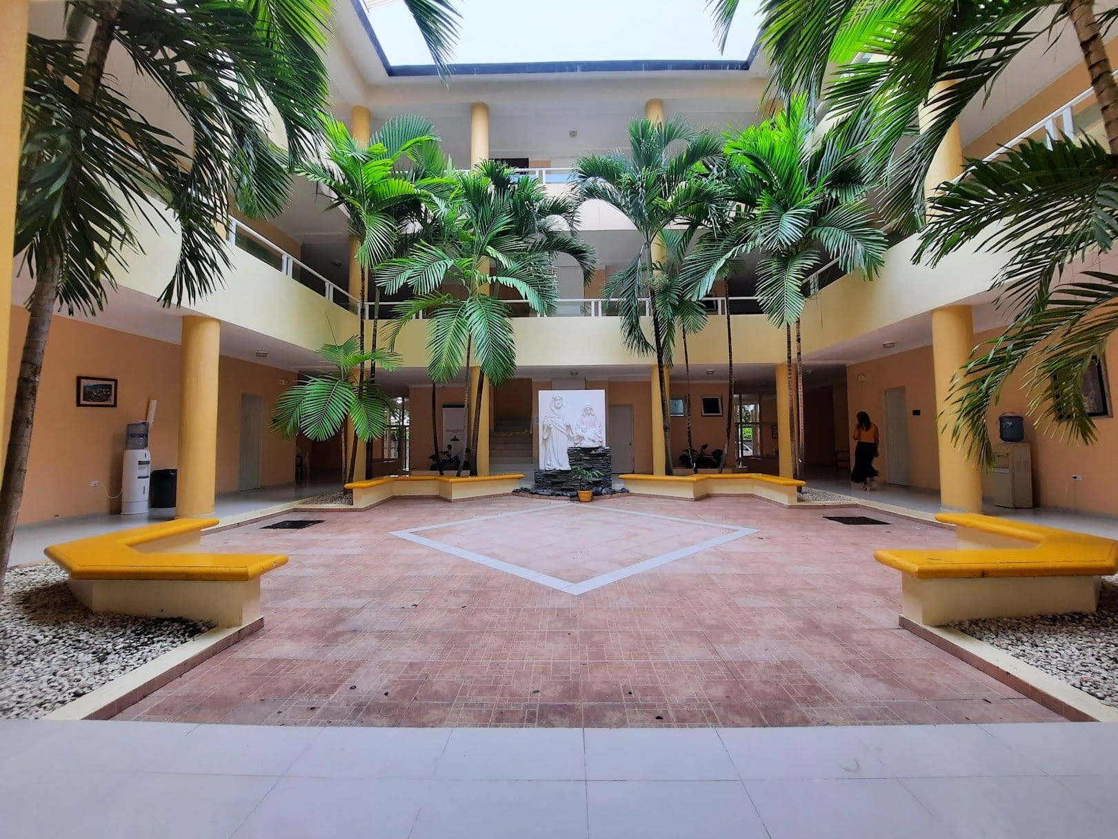 Patio interior del CEFIJUFA: dos niveles alrededor de un lucernario, con palmas, bancos y una imagen religiosa al fondo